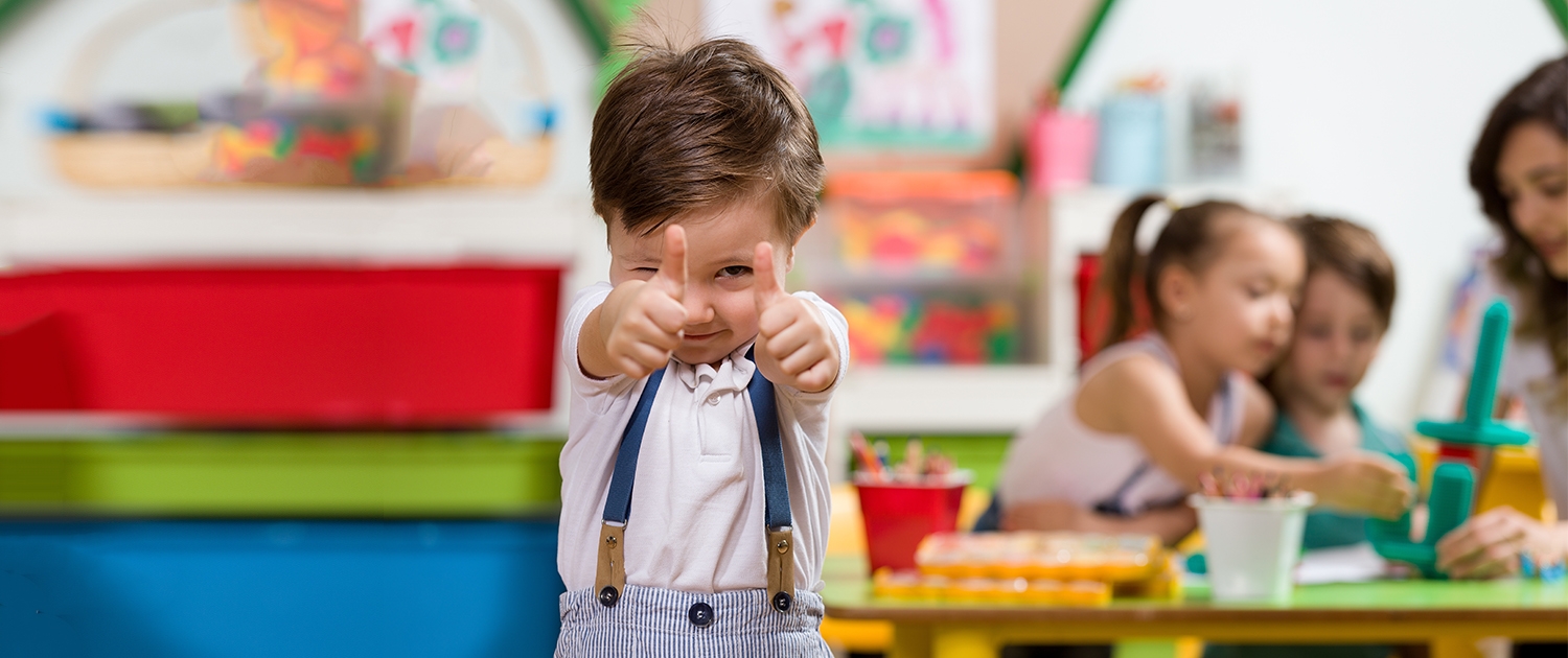 Ein kleiner Junge der aus einem Kindergarten,  mit beiden Händen "Daumen hoch zeigt".