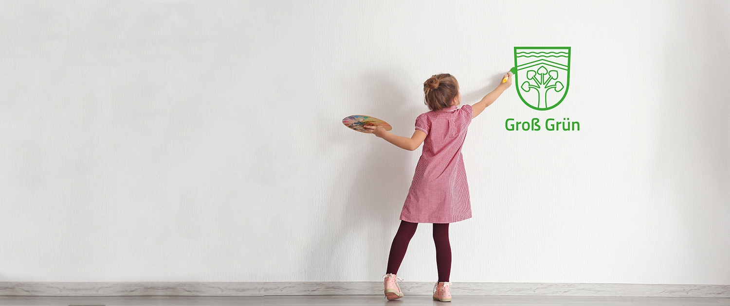 Ein kleines Mädchen mahlt das "Groß Grün" Logo auf eine weiße Wand. (Ein Bild zur Bildungslandschaft)