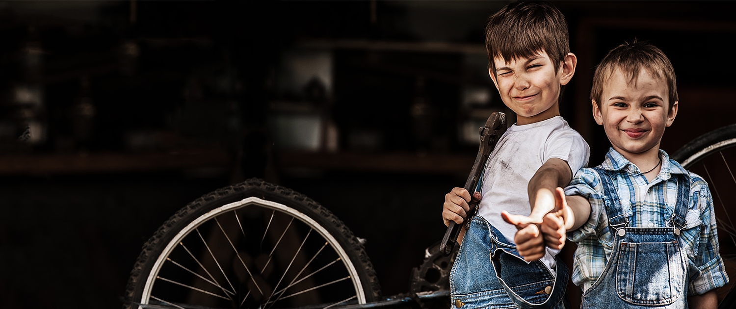 Zwei Kinder zeigen den Daumen hoch und der eine hat ein Schraubenschlüssel in der Hand. Im Hintergrund ist ein Fahrrad mit einem Defekten Reifen.