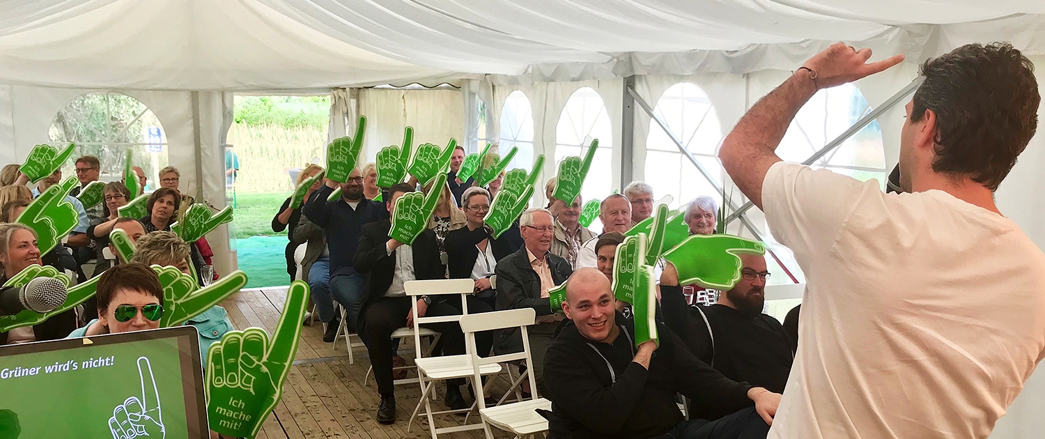 Eine Veranstaltung von "Grüner wird's Nicht". mehrere Personen sitzen in einem größeren Zellt und hören dem Veranstalter zu.