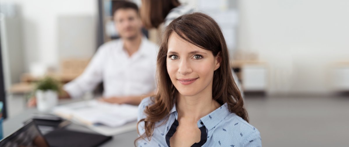 Eine Frau steht im Vordergrund und im Hintergrund sitzt ein Mann.