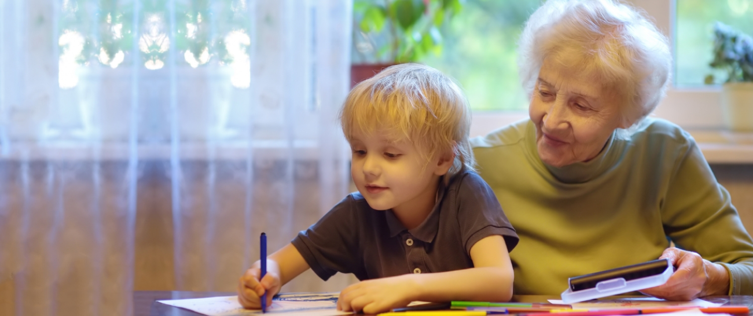 Eine Ältere Frau hilft einem Kind bei den Hausaufgaben.