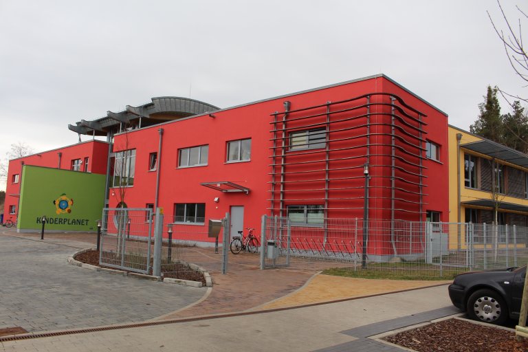 Das Gebäude von der Kita Kinderplanet in Blankenfelde mit einer roten, grünen und orangen Fassade.