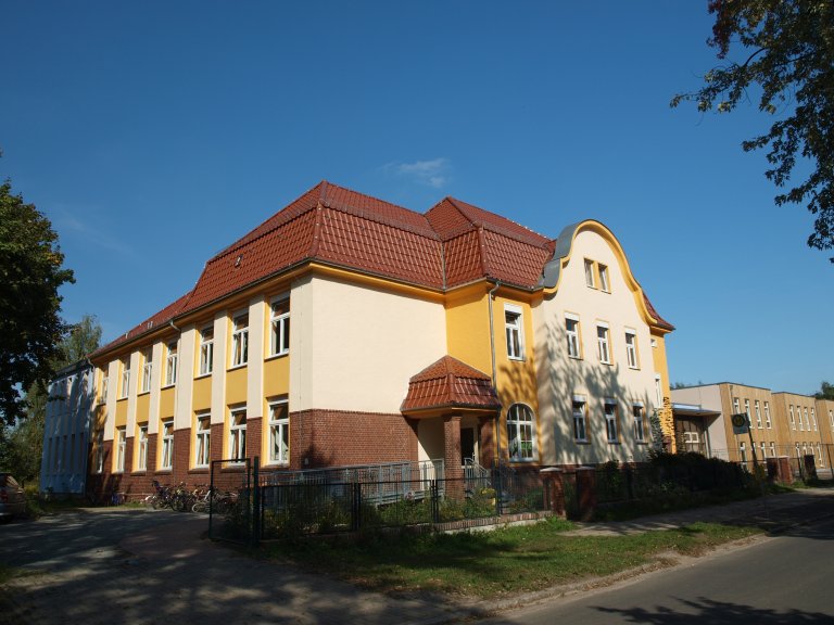 Das Gebäude der Evangelischen Grundschule in Mahlow, mit gelber Fassade und Roten Dachziegeln.