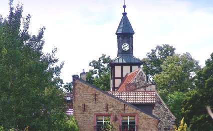 im Vordergrund ein Wohnhaus und im Hintergrund sieht na die Glasower Dorfkirche