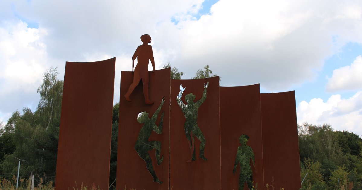 Mauerdenkmal "Erinnerung braucht einen Ort" Fünf Bronzesäulen mit Bronzefiguren die versuchen über die Mauer zu Klettern.
